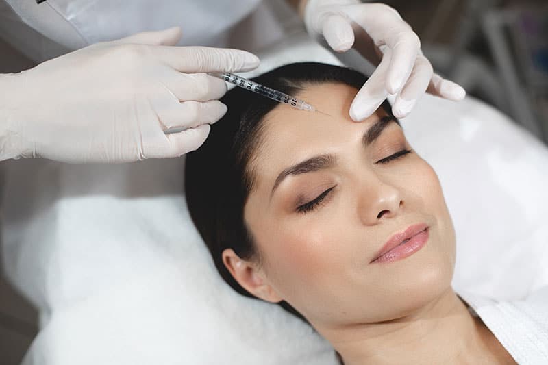 Young woman lying with closed eyes during botox injection process