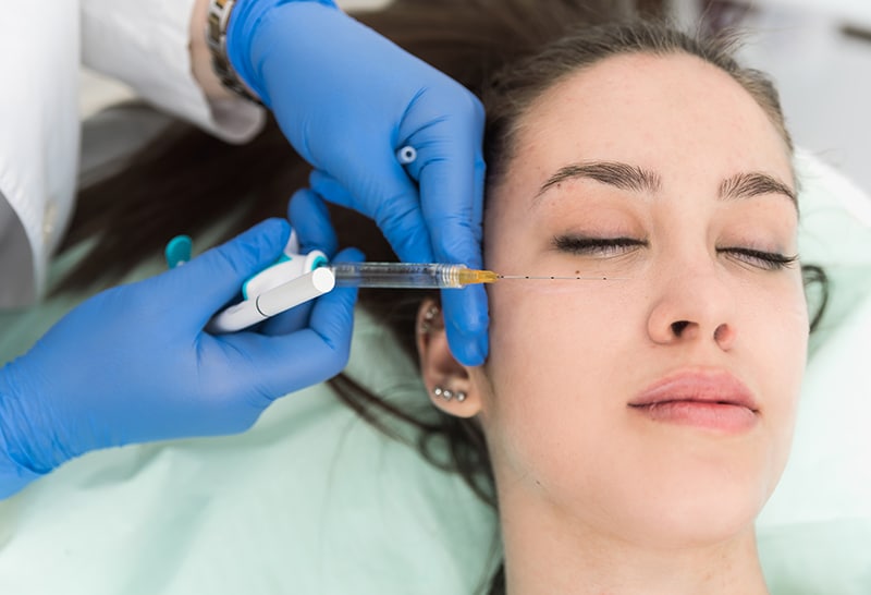 practitioner wearing hospital gown with patient under eye dermal filler practitioner wearing hospital gown with patient under eye dermal filler